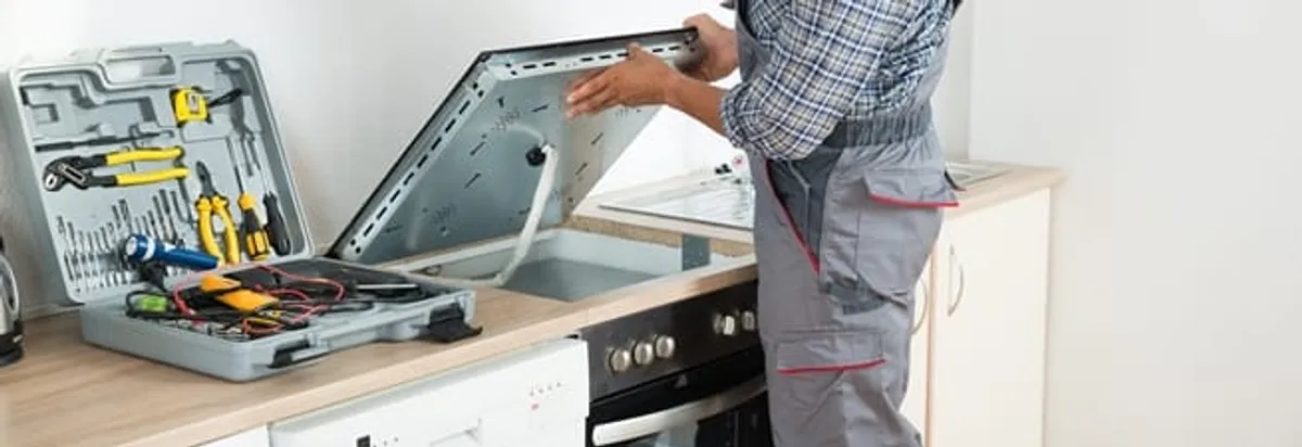 Cooktop repair technician lifting a built-in stovetop for service in Newark, NJ